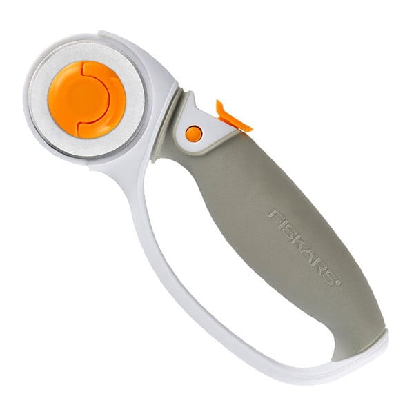 Nóż krążkowy Fiskars 1003861 z tytanowym ostrzem o średnicy 45 mm. Uchwyt w kolorze szarym z pomarańczowymi akcentami, ergonomiczny kształt, widoczny przycisk blokady ostrza. Ujęcie z boku, stojący.