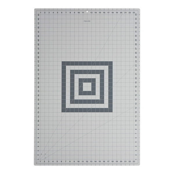 Mata podkładowa Fiskars A1 samogojąca o wymiarach 600x910x2mm, w kolorze szarym, z siatką milimetrową oraz wzorem w formie koncentrycznych kwadratów. Ułożona płasko na jasnym tle.