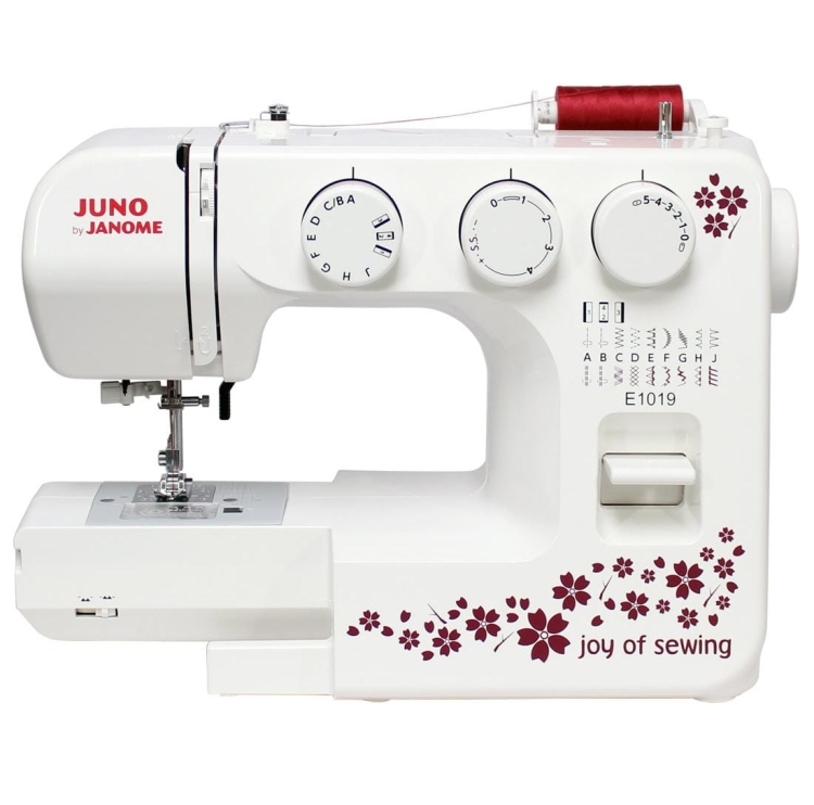 Maszyna do szycia Janome JUNO E1019 w kolorze białym z dekoracyjnym wzorem w czerwone kwiaty. Wyposażona w pokrętła do ustawiania ściegów oraz widoczny stół do szycia. Zestaw zawiera również dodatkowy element, widoczny na zdjęciu.