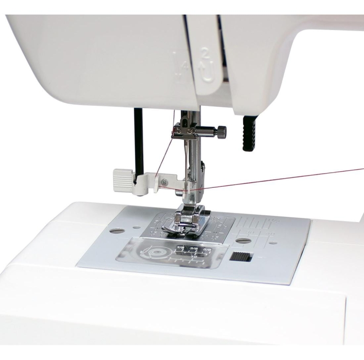 Maszyna do szycia Janome JUNO E1019 z widoczną stopką i igłą, z nitką przewleczoną przez oczko. Na metalowej płytce szereg oznaczeń do szycia. Produkt w białej obudowie, ukazany z bliska, w pozycji roboczej.