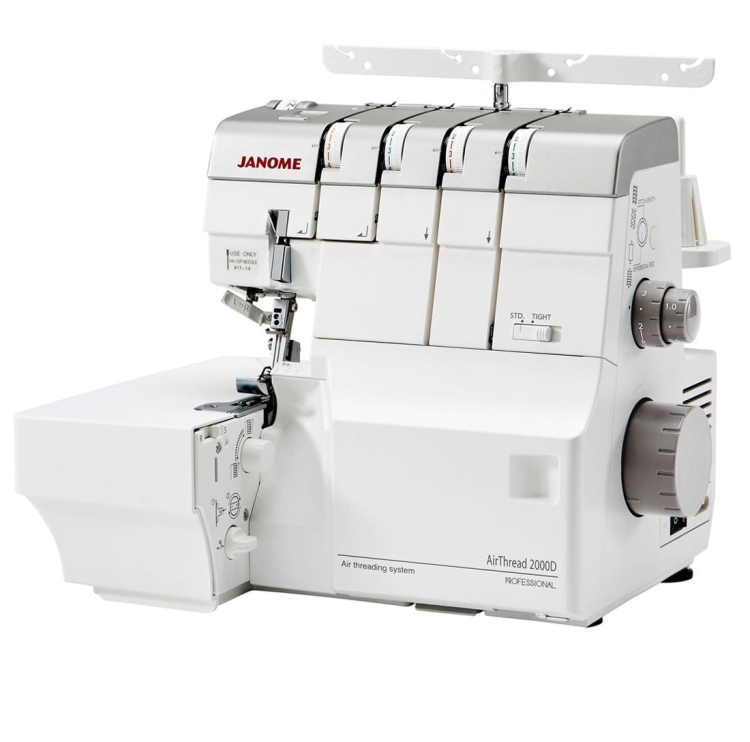 Owerlok Janome AT2000D Professional w kolorze białym, z systemem nawlekania powietrznego. Widoczny stół roboczy, pokrętła do regulacji oraz cztery szpulki z nicią. Maszyna stoi w pozycji otwartej, gotowa do pracy.