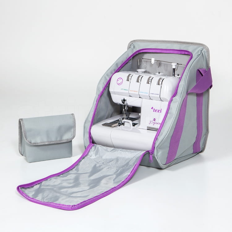 Torba na owerlok ENJOY BAG w kolorze szarym z fioletowymi akcentami, otwarta, z widoczną maszyną do szycia wewnątrz. Obok znajduje się mała, szara saszetka. Torba ma miękką fakturę i zamknięcie na zamek.