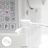 Lampka LED TEXI do maszyn szwalniczych, z 12 diodami, zasilana przez USB. Widoczny kabel podłączony do maszyny, złącze białe. Ujęcie z boku, na tle maszyny, z czytelnymi przyciskami panelu sterującego.