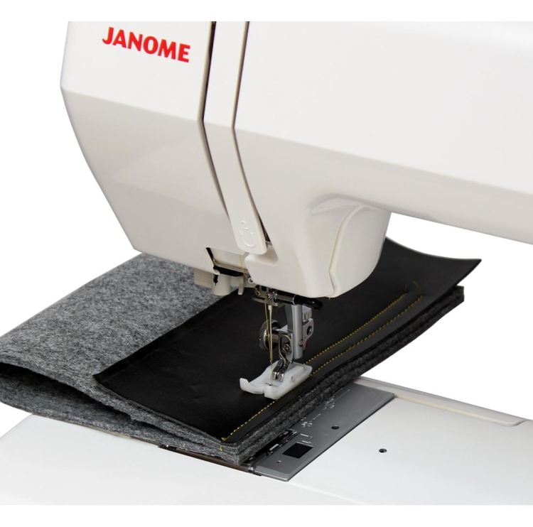 Maszyna do szycia Janome HD1800 z widocznym białym korpusem, zbliżenie na igłę i stopkę, szyjąca czarny materiał z żółtą nicią. Pod spodem znajduje się szary filc. Na obudowie logo Janome w czerwonym kolorze.