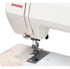 Maszyna do szycia Janome HD1800 Easy Jeans w białej obudowie, z metalowym stelażem. Widać igłę i stopkę, pracującą na jasnym materiale z wzorem kwiatowym. Panel sterujący z ikonami i oznaczeniami, umieszczony na blacie.