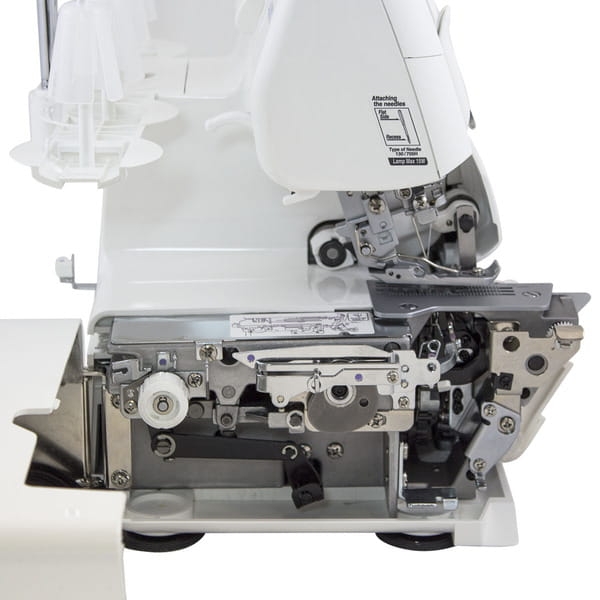 Coverlok JUKI MO-735 to overlok z funkcją renderki, widoczny z boku. Biała obudowa, metalowe elementy wewnętrzne, widoczny mechanizm szycia i instrukcje montażu. Na zdjęciu brak dodatkowych akcesoriów.