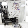 Maszyna overlock JUKI MO-735 z widoczną funkcją renderki. Biały korpus z instrukcją użytkowania na obudowie. Widoczne elementy mechaniczne, w tym igły, nici oraz uchwyt. Kąt ujęcia z boku, ukazujący szczegóły wnętrza urządzenia.