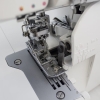 Coverlok JUKI MO-735 z metalową stopką, widoczny mechanizm szyjący z dwoma igłami, dolny chwytacz, regulacja naprężenia nici. Stojąca maszyna z białą obudową na tle jasnej powierzchni, idealna do szycia i renderowania materiałów.