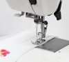 Maszyna do szycia Janome HD 523 EASY JEANS z bliska, z widoczną stopką i igłą w trakcie szycia białej tkaniny z kolorowym haftem. Ujęcie z góry, pokazujące detal szycia oraz metalową płytkę.