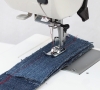Maszyna do szycia Janome HD 523 EASY JEANS w ujęciu z góry, z widoczną igłą i stopką, szyjąca grube kawałki denimu. Na materiale widać czerwoną nitkę. Tło jest jasne, a produkt leży na stole.