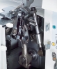 Zbliżenie na mechanizm owerloka Minerva M840DS, z widocznymi metalowymi elementami, trzema igłami oraz częściami roboczymi. Obok etykiety z instrukcją użytkowania i elementami regulacyjnymi. Tło białe, produkt w pozycji otwartej.