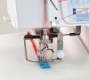 Coverlok Janome 1200D, overlock z funkcją renderki, z widocznym mechanizmem szyjącym, niebieską stopką i czerwonym szwem na białym materiale. Ujęcie z boku, pokazujące detale nici i ustawienia maszyny.