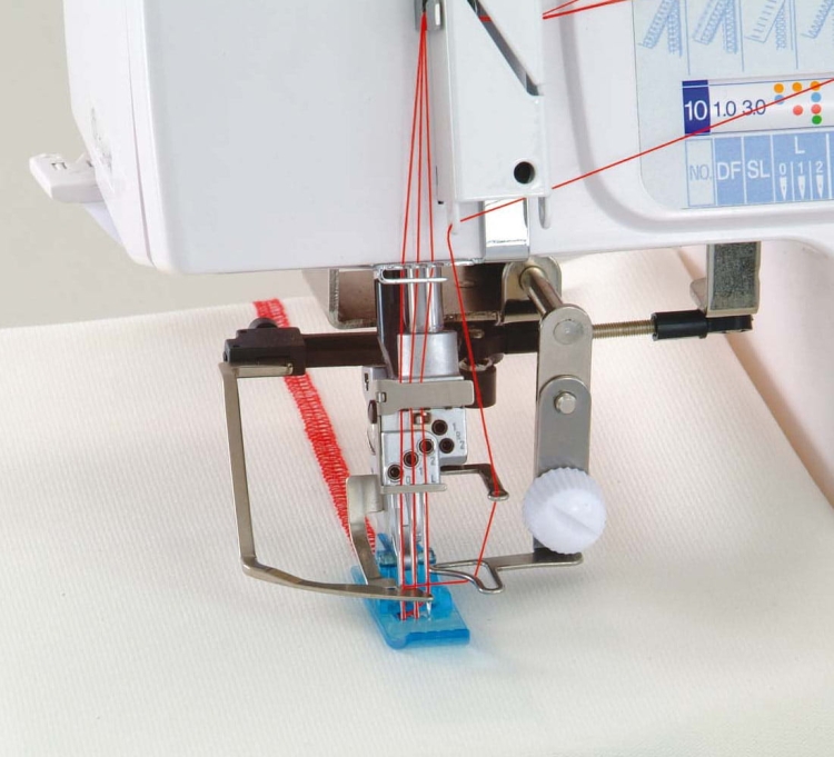 Coverlok Janome 1200D, overlock z funkcją renderki, z widocznym mechanizmem szyjącym, niebieską stopką i czerwonym szwem na białym materiale. Ujęcie z boku, pokazujące detale nici i ustawienia maszyny.
