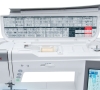 Maszyna do szycia Janome MC9450QCP, widok górny z otwartą pokrywą, pokazujący panel z symbolami ściegów. Wewnątrz szpula z jasnym nicią, przyciski sterujące po lewej stronie oraz wyświetlacz LCD z informacjami o ściegach.