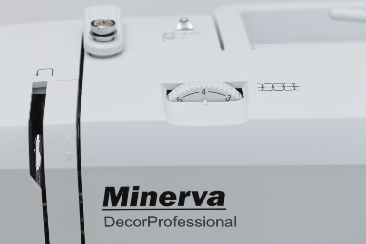 Maszyna do szycia Minerva DecorProfessional w kolorze białym z widocznym pokrętłem regulacji oraz logo producenta. Zbliżenie na panel kontrolny z oznaczeniami ściegów, ukazujące precyzyjne detale konstrukcji.