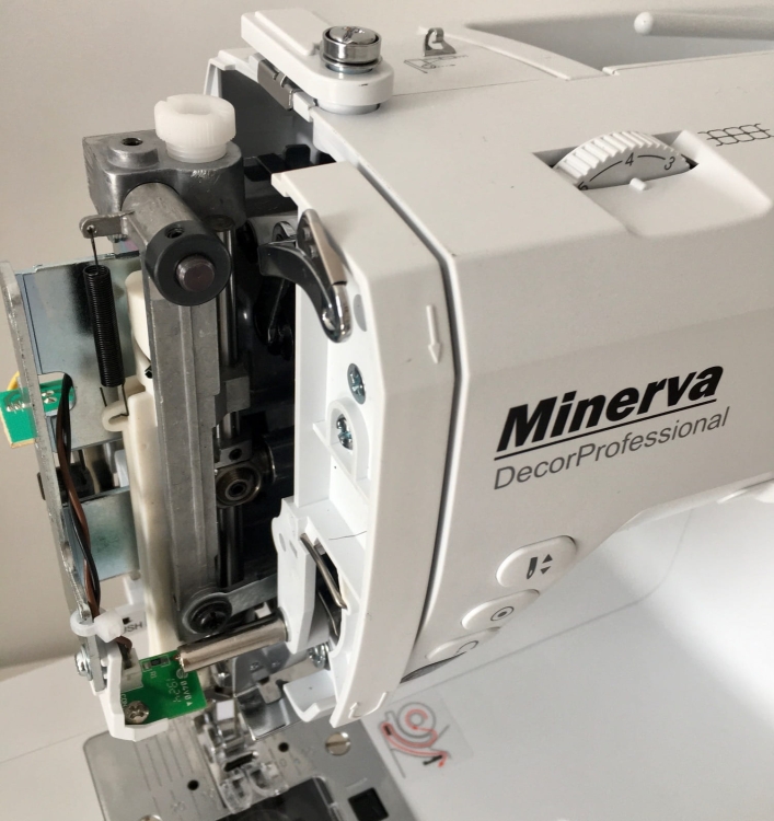 Maszyna do szycia Minerva DecorProfessional w kolorze białym, widok z boku. Zawiera widoczne elementy sterujące, w tym pokrętło i przyciski. Odsłonięty mechanizm pokazuje metalowe i plastikowe części, zapewniające precyzyjne szycie.