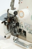 Częściowa widok na owerlok Minerva M640DS, ukazujący mechanizm 4-nitkowy, z widocznymi elementami metalowymi, w tym rolką i złożonymi nitkami. Na obudowie umieszczone instrukcje dotyczące nawlekania. W tle jasne, neutralne.