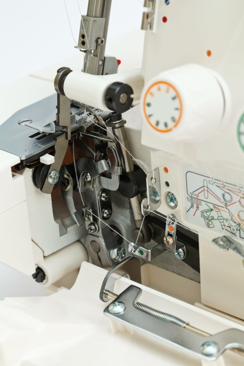 Częściowa widok na owerlok Minerva M640DS, ukazujący mechanizm 4-nitkowy, z widocznymi elementami metalowymi, w tym rolką i złożonymi nitkami. Na obudowie umieszczone instrukcje dotyczące nawlekania. W tle jasne, neutralne.