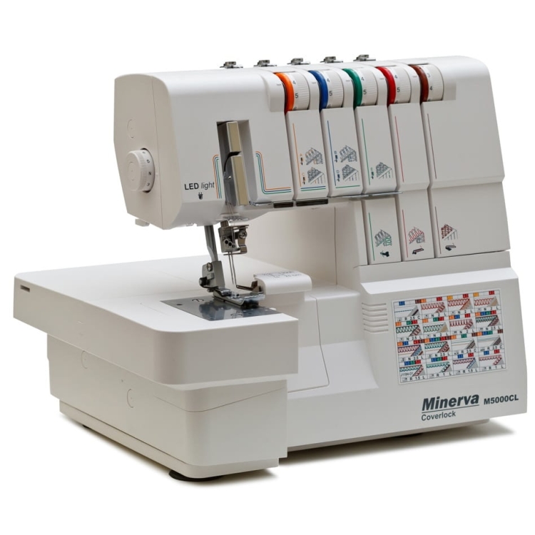 Coverlok Minerva M5000CL, maszyna do szycia w kolorze białym, z funkcją renderki. Widoczny stół roboczy, zamontowana stopka oraz sześć kolorowych szpul nici. Panele z instrukcjami szycia po prawej stronie oraz oświetlenie LED.