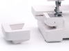 Coverlok Minerva M5000CL to biała overlock z funkcją renderki. Widoczny detal to odłączona część maszyny z prostokątnym otworem. Kąt ujęcia z boku, na białym tle, ukazuje konstrukcję i elementy funkcjonalne.