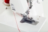 Renderka Juki MCS-1500 w kolorze białym, z widoczną stopką do szycia oraz igłami. Na zdjęciu zbliżenie na mechanizm z nitką w kolorze czerwonym, umiejscowiona na jednolitym tle. Widać także instrukcję dotyczącą mocowania igieł.