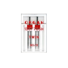 Igła podwójna półpłaska 130/705H Organ TWIN 90/3mm w przezroczystym opakowaniu, z dwoma metalowymi igłami połączonymi na górze. Widoczne napisy: ORGAN, 130/705H, TWIN, 90/3. Produkt przeznaczony do szycia.