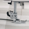 Uchwyt MATIC szybkomocujący do stopki Janome, wykonany z metalu, z widocznym mechanizmem mocującym oraz szpiczastą stopką. Produkt uchwycony w zbliżeniu, umieszczony na tkaninie w odcieniach szarości, z widocznym nicią.