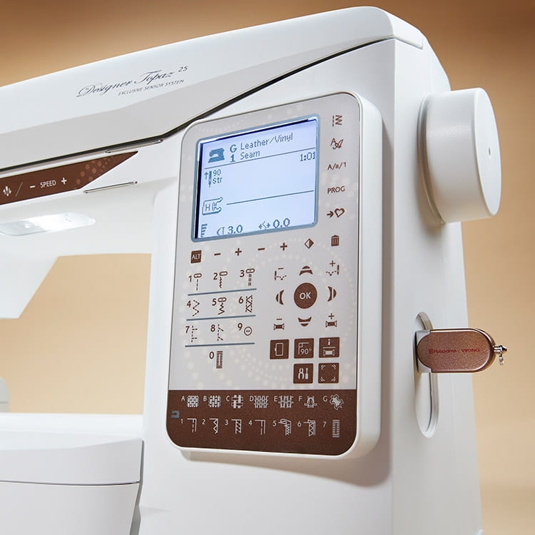 Maszyno-hafciarka Husqvarna Designer Topaz 25 z wyświetlaczem LCD, przyciskami i symbolami do wyboru ściegów. Widać port USB z logo Husqvarna, obudowa w kolorze białym z brązowymi detalami. Ujęcie zbliżeniowe, frontalne.