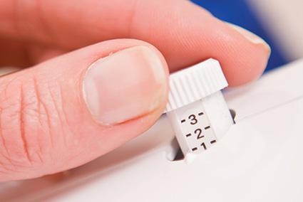 Zbliżenie na pokrętło regulacji owerloka Brother 4234D, z widocznymi oznaczeniami od 1 do 3. Ręka trzymająca pokrętło, które jest białe z wyraźnymi cyframi. Tło w rozmyciu, co podkreśla szczegół produktu.