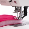 Maszyna do szycia PFAFF QUILT AMBITION 630, widok z bliska na stopkę i igłę, szyjąca różowy materiał z ociepliną. Widoczny podwójny transport i panel sterowania. Tło białe.