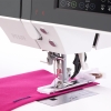 Maszyna do szycia PFAFF QUILT AMBITION 630 z podwójnym transportem, widoczna z bliska, z igłą i stopką na różowym materiale. Na panelu sterującym znajdują się przyciski i wyświetlacz z ustawieniami. Widać także mechanizm transportu tkaniny.