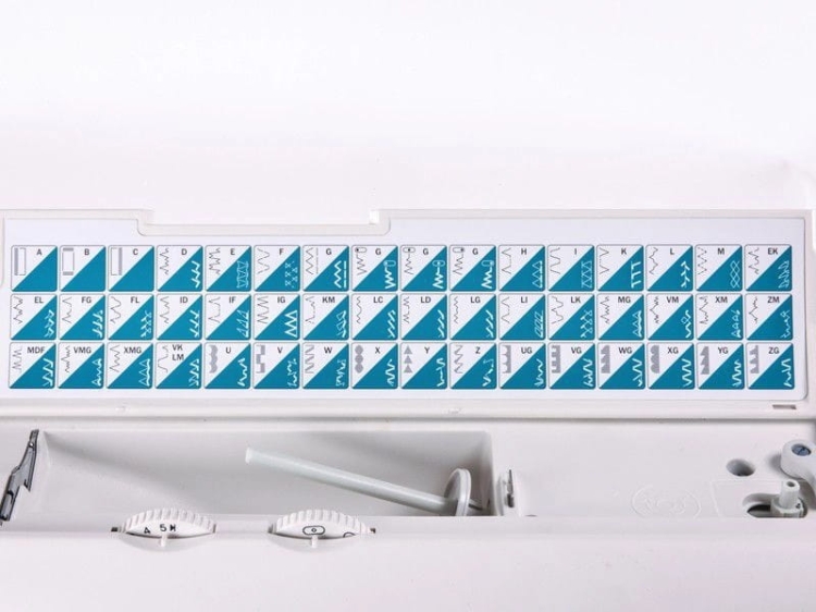 Panel maszyny do szycia Gritzner Tipmatic 6152 z podwójnym transportem, ukazujący różne wzory ściegów w kolorze niebieskim i białym. Widoczne pokrętła do regulacji oraz miejsce na szpule. Tło białe, prezentujące elementy w zbliżeniu.