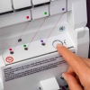 Coverlok PFAFF ADMIRE AIR 7000 z systemem łatwego nawlekania, pokazany z bliska. Widoczne pokrętło z ikoną nawlekania, kolorowe oznaczenia nici oraz przycisk w ręce użytkownika. Tło w jasnym kolorze, elementy instrukcji widoczne na obudowie.
