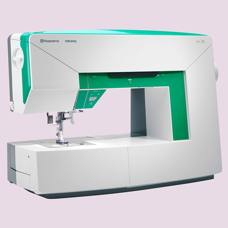 Maszyna do szycia Husqvarna Viking Jade 20 w kolorze białym z zielonymi akcentami. Ujęcie z boku, pokazujące panel sterujący z przyciskami i igłę. Produkt stoi na płaskiej powierzchni, z widocznym miejscem na materiał do szycia.