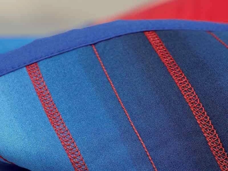 Coverlok Redstar 5.0, owerlok z funkcją renderki, w kolorze niebieskim z czerwonymi detalami. Zbliżenie na szwy, ukazujące precyzyjne pikowanie i teksturę materiału. Produkt leży na jednolitym tle, uwydatniając jego funkcjonalność i design.
