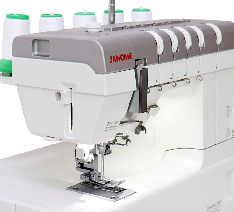 Renderka Janome CP3000P w kolorze białym z szarym elementem, z widocznymi szpulami nici. Widać mechanizm szycia oraz stopkę. Produkt stoi na płaskiej powierzchni, zbliżenie na detal maszyny.