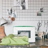 Maszyno-hafciarka Husqvarna Viking DESIGNER JADE 35 w kolorze białym z zielonymi akcentami, z widocznym haftem na zielonym materiale. Ujęcie z boku, na stole z dodatkami jak lampka, nożyczki i zdjęcia na tle siatki.