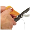 Nożyczki wielofunkcyjne Fiskars Cuts+More 1000809 mają żółty uchwyt z ergonomiczną formą i czarne ostrze. Na zdjęciu ukazano rękę trzymającą nożyczki, które tną cienki drut. Ujęcie z bliska, skupione na detalu użycia.