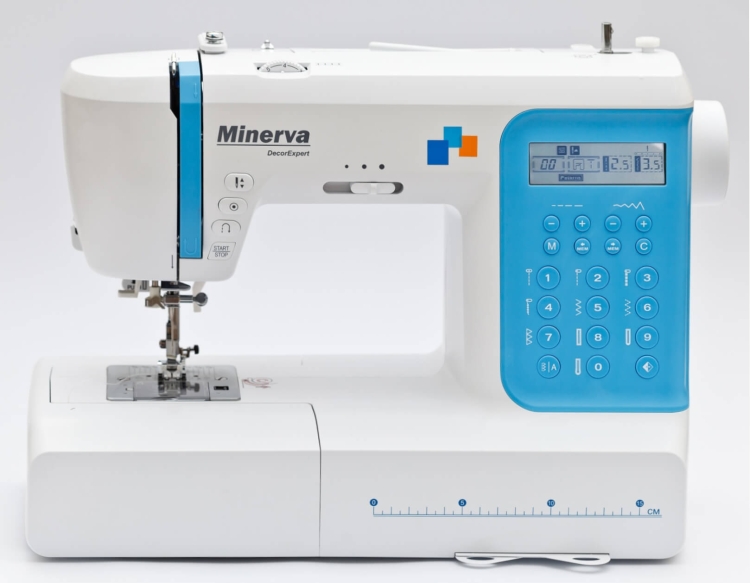 Maszyna do szycia Minerva DecorExpert w kolorze białym z niebieskimi akcentami. Wyposażona w panel sterujący z przyciskami oraz wyświetlaczem. Widoczny stół maszyny z metalową stopką. Kąt ujęcia frontalny, na jednolitym tle.