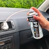 Środek do odgrzybiania klimatyzacji w sprayu 400 ml Spirit 64 trzymany w dłoni, z elastyczną rurką skierowaną w stronę kratki wentylacyjnej. Produkt znajduje się na desce rozdzielczej samochodu. Tło stanowi zielony żywopłot.