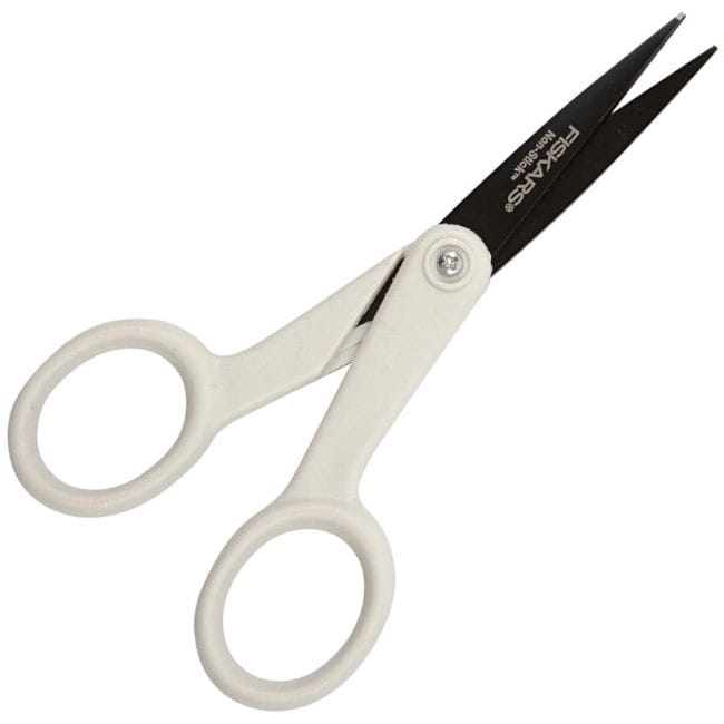Nożyczki uniwersalne Fiskars Non-stick 1004682 o długości 12 cm, z białymi uchwytami i czarnymi ostrzami. Ujęte frontalnie, otwarte, z widocznym logo. Ostrza wykonane z materiału zapobiegającego przywieraniu.