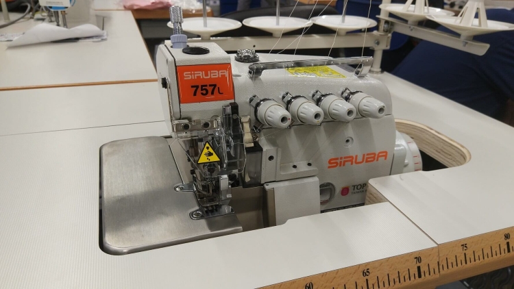 Owerlok SIRUBA 757L-516M3-55/DKLU 5-nitkowy w kolorze szarym z pomarańczowymi detalami. Ujęcie z boku, pokazujące maszyny z widocznymi trzema białymi nawlekaczami i metalowym blatem. Na obudowie znajduje się logo i oznaczenia.