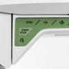 Panel sterujący maszyny do szycia Husqvarna Viking Tribute 150C z przyciskami START/STOP, STOP, FIX na zielonym tle. Widoczne są także strzałki oraz symbol nawrotu. Kąt ujęcia z bliska, ukazujący detale przycisków i ich oznaczenia.
