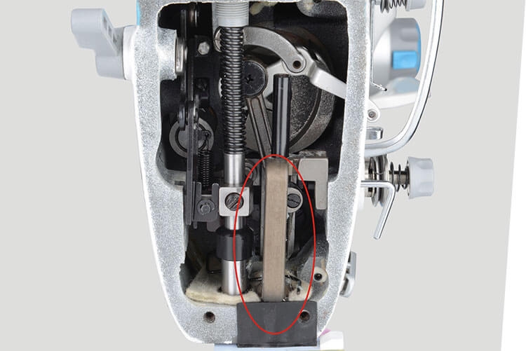 Widok wewnętrzny stebnówki JACK A6F-E, ukazujący mechanizm z transportem ząbkowo-igłowym. Widoczne elementy metalowe prowadnice, sprężyny oraz zębatki, które odpowiadają za automatyczne przesuwanie materiału. Całość w kolorze srebrnym z detalami czarnymi