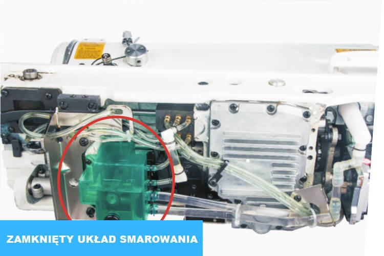 Zygzak JACK JK-2T290D-SR z widocznym zamkniętym układem smarowania. Zbliżenie na zielony element, przezroczyste wężyki oraz metalowe komponenty maszyny. Kąt ujęcia z boku, na jasnym tle.