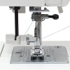 Nawlekacz igły do maszyn JUNO J15R, E1019, E1030, Janome 1522 i Elna 220, 240, widoczny z bliska, umieszczony przy igle maszyny. Metalowa stopka i szara płytka z oznaczeniami, igła z nitką, wyraźnie widoczna w centralnej części.