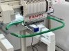 Hafciarka KRAFFT KF-CT1501H, jednogłowicowa, 15-igłowa, z zielonym obrębem do haftu. Widok z boku, z bliska na głowicę maszyny z logo KRAFFT oraz mechanizmem igieł. Tło jasne, stół roboczy w kolorze białym.