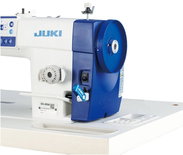 Stebnówka JUKI DDL-8000A-MS, jednolita, automatyczna maszyna do szycia z niebieskimi i białymi elementami, widoczny mechanizm, pokrętło do regulacji, włącznik, montaż na stabilnym blacie. Przeznaczona do lekkich i średnich materiałów.