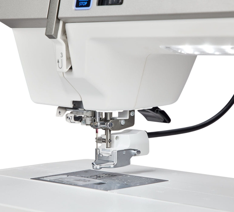 Maszyna do szycia Janome MC9480QCP Professional w zbliżeniu, pokazująca stopkę do szycia, igłę oraz panel sterujący. Biała obudowa, metalowe elementy, widoczny stół z oznaczeniami na powierzchni. Idealna do precyzyjnego szycia.