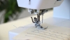 Maszyna do szycia BERNETTE Sew&Go 5 w zbliżeniu, z widoczną stopką, igłą oraz niebieską nicią szyjącą. Na materiale widać równo ułożone ściegi, a całość umieszczona na jasnym tle.